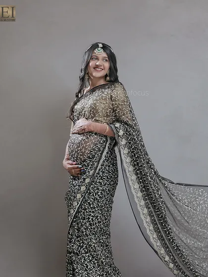 An elegant shot of a mom-to-be in a sheer black embroidered saree, with the fabric flowing beautifully.