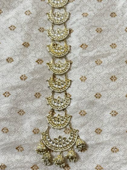 A delicate hair choti accessory with half-moon Kundan pieces and pearl detailing. This rental piece adds elegance to your hairstyle.