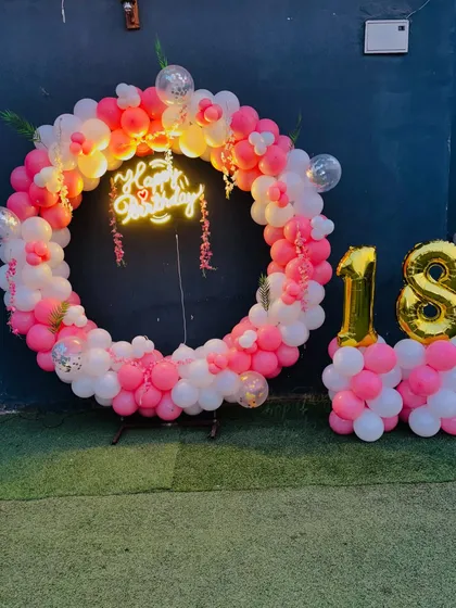 An 18th birthday celebration with a pink and white balloon ring, a neon sign, and large gold foil number balloons.