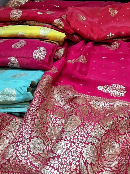 A beautiful spread of our festive collection sarees. You can see the variety of colors we offer, from bright pink and yellow to a serene sky blue, all featuring classic Banarasi butti and border designs.