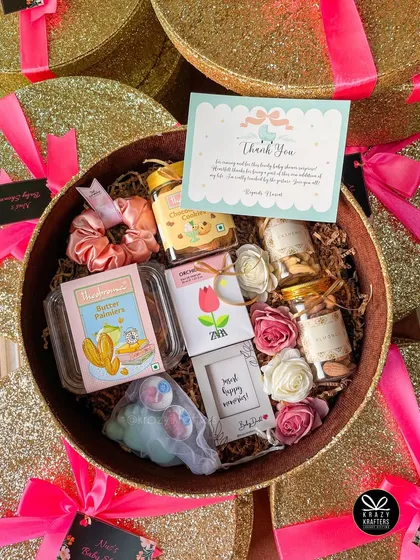 A look inside one of the glam baby shower favor boxes. It's filled with treats, a satin scrunchie, a mini frame, and other goodies for the guests to take home.