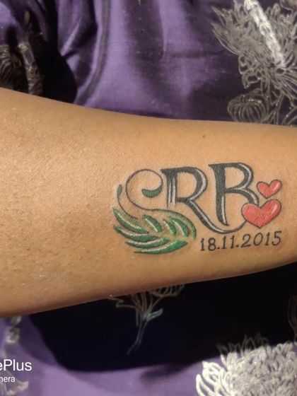 This tattoo combines the initials "SRB" with a special date, two hearts, and a small leaf design. It's a great example of how we can merge multiple meaningful elements into one piece.