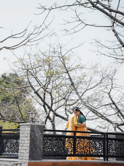 A couple shares a quiet hug on a balcony, framed by bare tree branches, during their Haldi celebration in the hills.