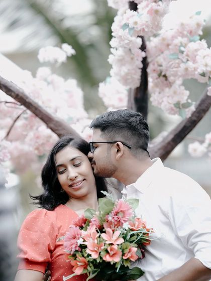 A tender moment with the groom kissing the bride's cheek under a canopy of pink blossoms.