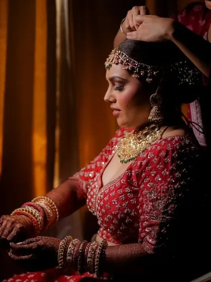 A dramatic getting-ready shot of the bride, with a helper adjusting her hair. The chiaroscuro lighting adds a timeless, painterly quality.