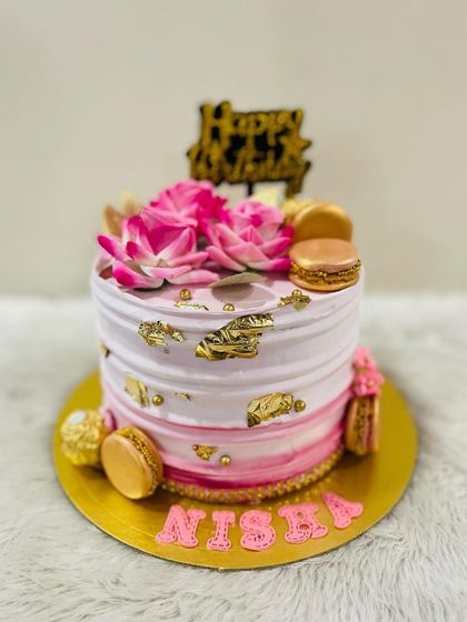 A beautiful pink ombre cake with gold leaf accents, topped with lotus flowers and golden macarons.