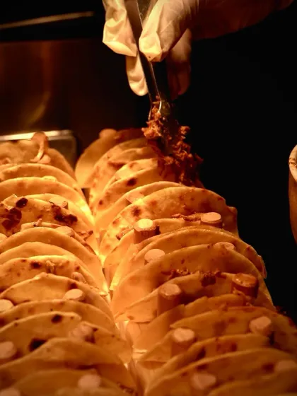 A close-up action shot of a taco being filled with savory meat. The focus on the food highlights the freshness and generous portions that make our taco bar a guest favorite.