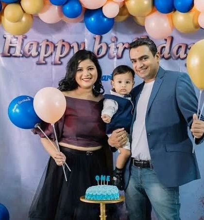 A happy family of three celebrating their son's first birthday. They pose with balloons and a cake, marking this important milestone.