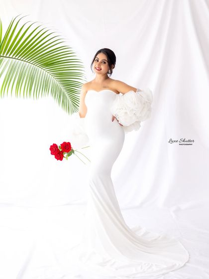 A full-length portrait in a white gown against a bright, clean background, with a palm leaf adding a touch of tropical elegance.