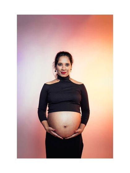A confident studio portrait of an expectant mother in a black outfit, holding her belly. The warm, gradient background adds a modern and artistic touch.