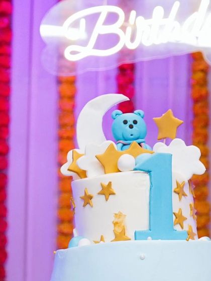A close-up of a beautifully decorated first birthday cake, featuring a "twinkle twinkle little star" theme with a teddy bear, moon, and stars.