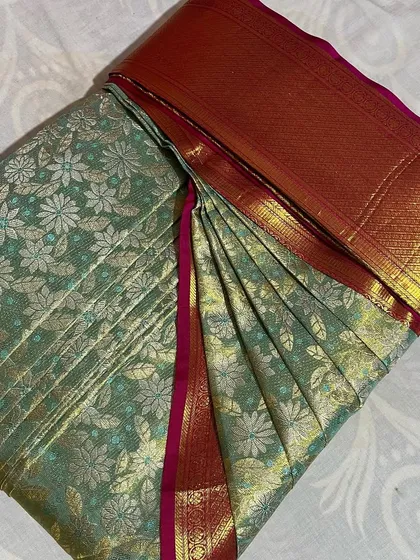 A light green floral saree with a red and gold border, folded with care.