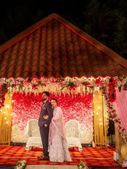 A full-view shot of the couple against their beautiful red and white floral reception stage.