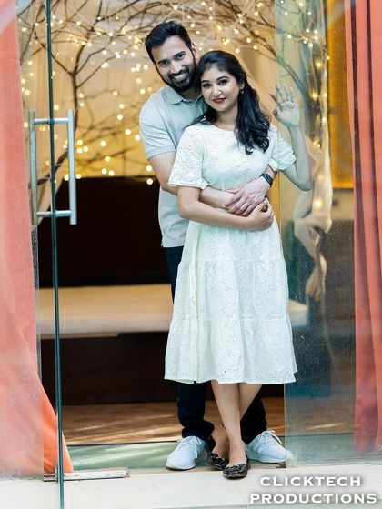 A happy and welcoming pose, with a couple embracing and waving from a doorway decorated with fairy lights.