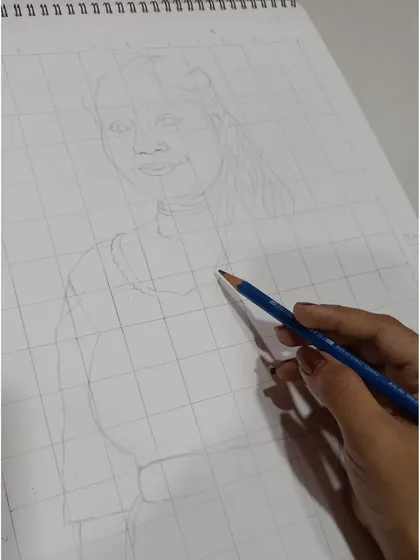The very first step: my hand sketching the initial outline on a gridded sheet of paper, laying the groundwork for the detailed portrait.