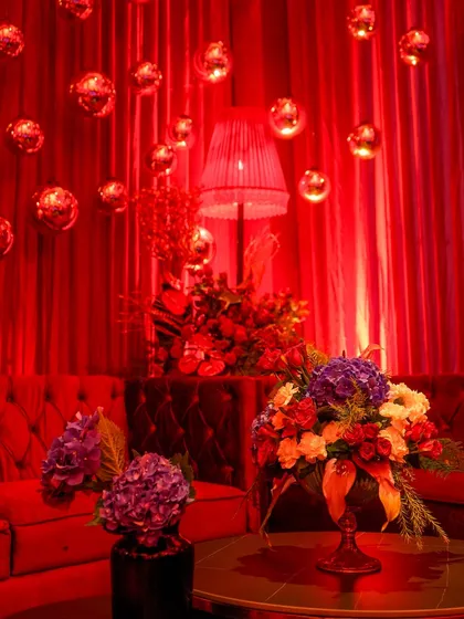 A lounge area within the party, featuring a plush red velvet sofa, a floral arrangement with pops of purple, and floating disco balls against a red curtain backdrop. The mood was pure glamour.