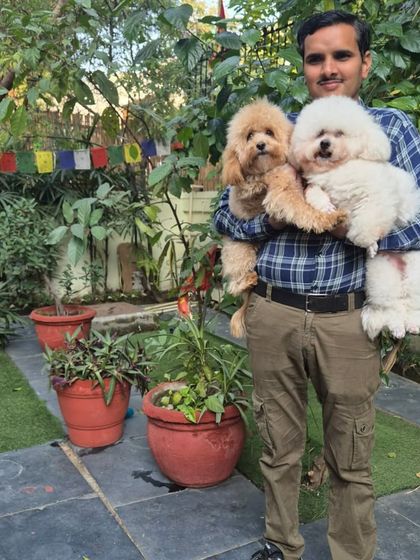 Our team member Narain holding Archie and Columbus. The lush green background shows our well-maintained outdoor space where dogs can play and relax.