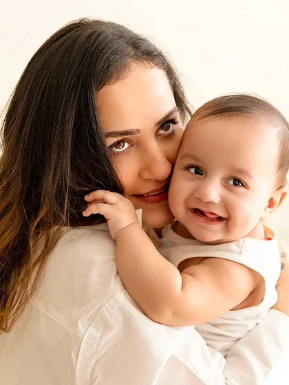 A mother holds her smiling baby boy, a perfect example of a mother and child portrait. The simple white outfits keep the image bright and fresh.