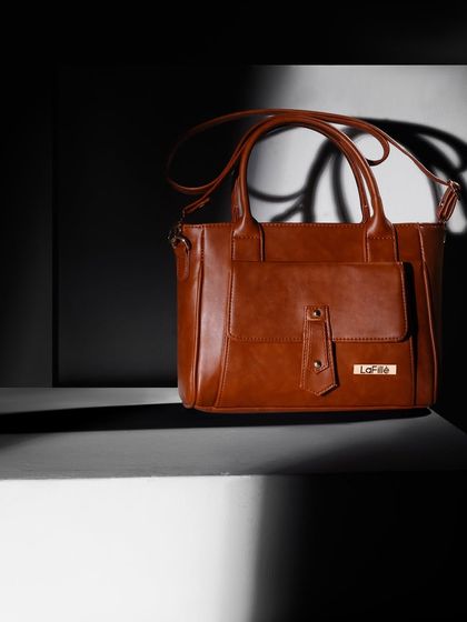 A classic tan handbag shot with dramatic, high-contrast lighting. The play of light and shadow accentuates the bag's structure and details.
