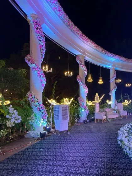 A side angle of the grand reception stage, showing how the curved structure is decorated with flowers and drapes. The hanging chandeliers and illuminated floral stands create layers of beautiful light.