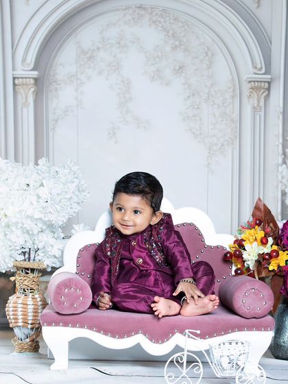 This little one is looking regal in his purple outfit, sitting on a pink sofa.