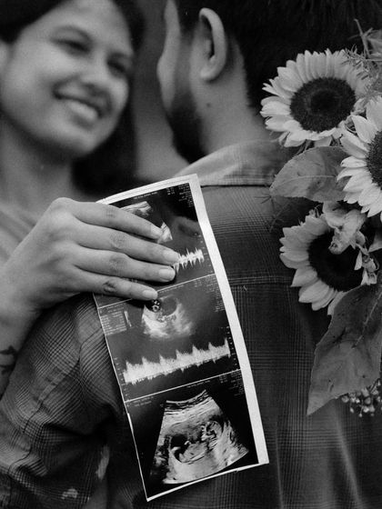 A black and white close-up that is both artistic and emotional. The sonogram is held against his back as they embrace, a creative way to include their baby in a romantic shot.