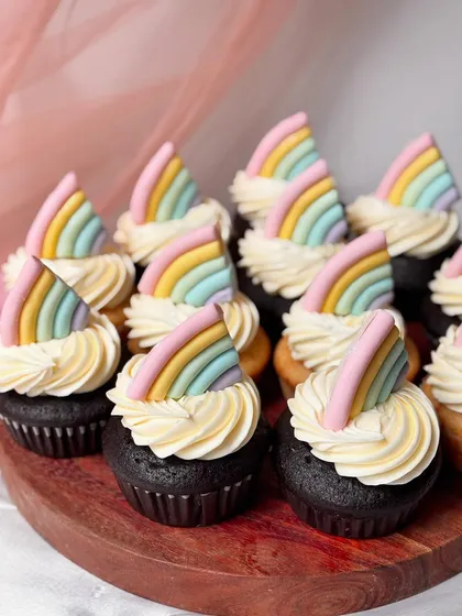 A batch of chocolate and vanilla cupcakes topped with classic buttercream swirls and a pastel rainbow fondant piece. This simple yet popular rainbow theme is great for birthdays, pride celebrations, or any cheerful event.