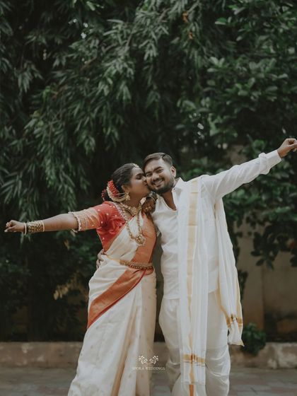 A joyful shot of the bride giving her groom a kiss on the cheek, both with their arms outstretched in celebration.