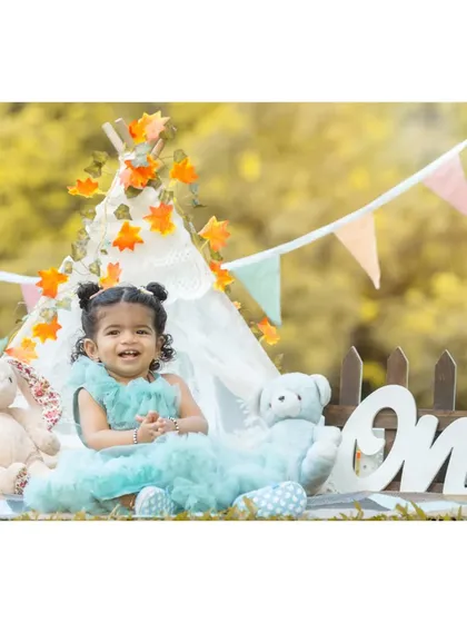 A happy smile from the birthday girl. Nitya is surrounded by her favorite teddy bears in this shot from her first birthday celebration, dressed in a lovely blue party dress.