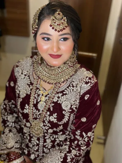 A classic portrait of a bride in a deep maroon velvet outfit. The makeup features a flawless base, soft smokey eyes, and a matching lip color, creating a look of pure elegance.