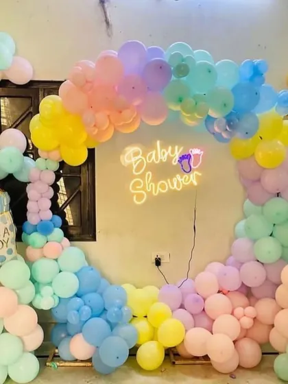 A pastel rainbow 'Baby Shower' decoration with a circular balloon arch and a neon sign.