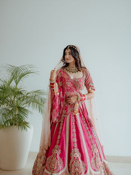 A stunning bridal portrait, capturing the bride in her magnificent pink lehenga, looking away with a gentle, thoughtful expression.