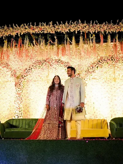 A wide shot of the couple on their grand floral stage. The hanging flower arrangements and the wall of flowers create a breathtaking backdrop that exudes romance and opulence.