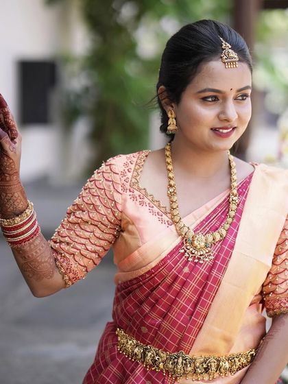 A close-up of Divya, ready for her event. Her makeup is soft and natural, with a pretty pink lip that complements her peach and red saree.