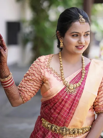 A close-up of Divya, ready for her event. Her makeup is soft and natural, with a pretty pink lip that complements her peach and red saree.
