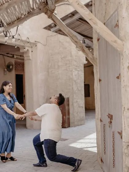 A playful moment in the historic Al Seef district of Dubai, where he kneels before her. This candid shot captures the fun and spontaneity of their relationship.