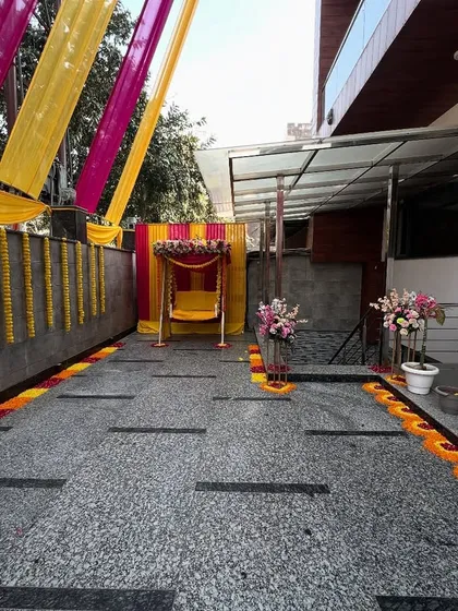 A full view of a home's driveway decorated for a pre-wedding function, with a decorated swing, marigold garlands, and a flower petal walkway.