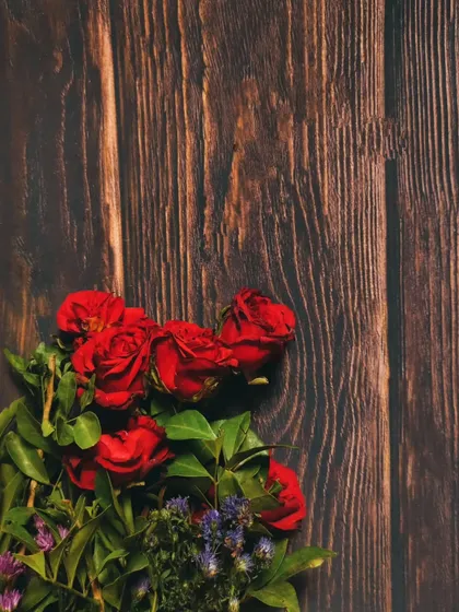 A minimalist composition of red roses on a dark wood background, using negative space to create a simple yet elegant image.