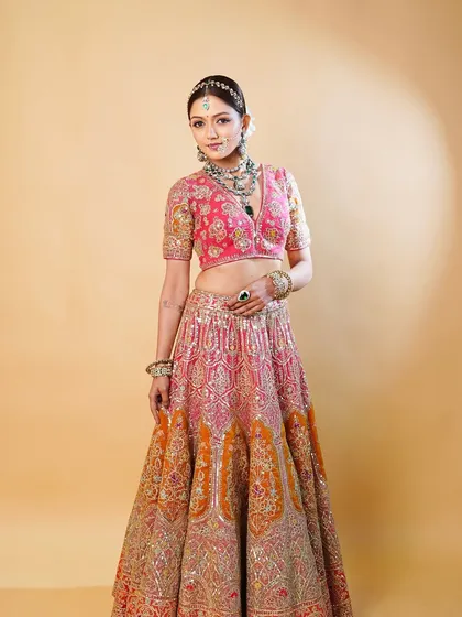 A full view of the bride in her stunning pink and tangerine lehenga. The makeup provides a radiant glow that ties the entire regal ensemble together.
