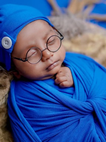 A close-up of our little dreamer. The details of the blue swaddle, buttoned cap, and tiny glasses come together for a perfectly themed shot.