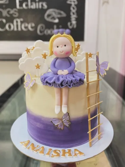 A dreamy cake featuring a fondant doll sitting among the clouds. The purple ombre effect and golden ladder add to the enchanting feel of this design.