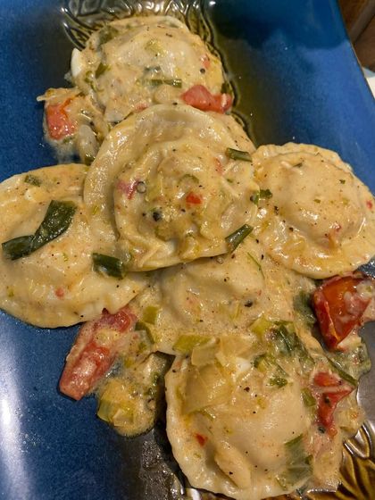 A close-up of our creamy ravioli. Each pasta pocket is filled with a savory mixture and coated in a luscious sauce with fresh herbs and tomatoes, perfect for an Italian-themed menu.