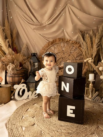 Standing tall by her 'ONE' blocks, this photo captures a proud first birthday moment. The detailed boho backdrop adds depth and texture to the image.