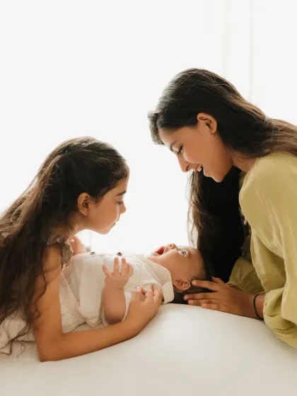 Two older sisters interact playfully with their baby brother. These candid moments are what make sibling photoshoots so special.