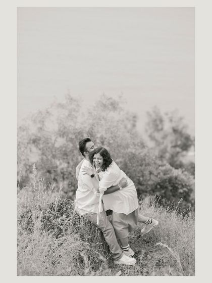 A playful, happy moment on a grassy hill. The black and white edit focuses on their joyful interaction and the texture of the landscape.