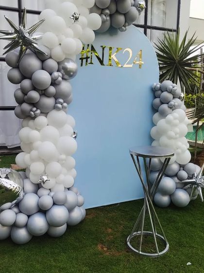An alternate angle of the modern outdoor balloon arch decoration. This view shows the depth of the silver and white balloon arrangement against the custom blue backdrop.