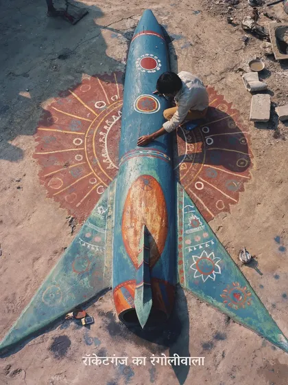 A boy paints a rangoli in the shape of a crashed rocket on the ground. This is a poignant image about how art and tradition persist and adapt even in a dystopian environment.