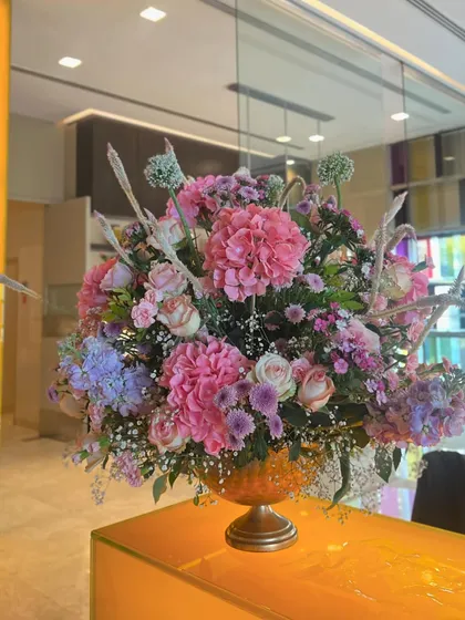 A large, opulent floral arrangement in a gold urn, featuring a mix of pink hydrangeas, roses, and other seasonal blooms. This statement piece added a touch of grandeur to the restaurant's decor.