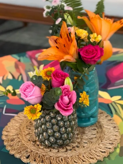 A fun and tropical centerpiece for a pool party, using a pineapple as a vase for a colorful floral arrangement.
