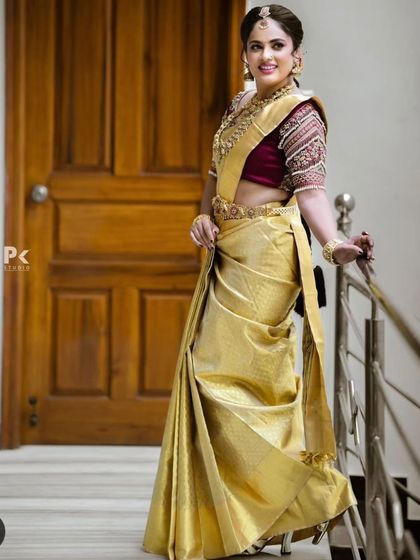 A full-length shot of a bride in a golden silk saree, wearing a traditional temple jewellery set. This is a classic and elegant look for a South Indian wedding.